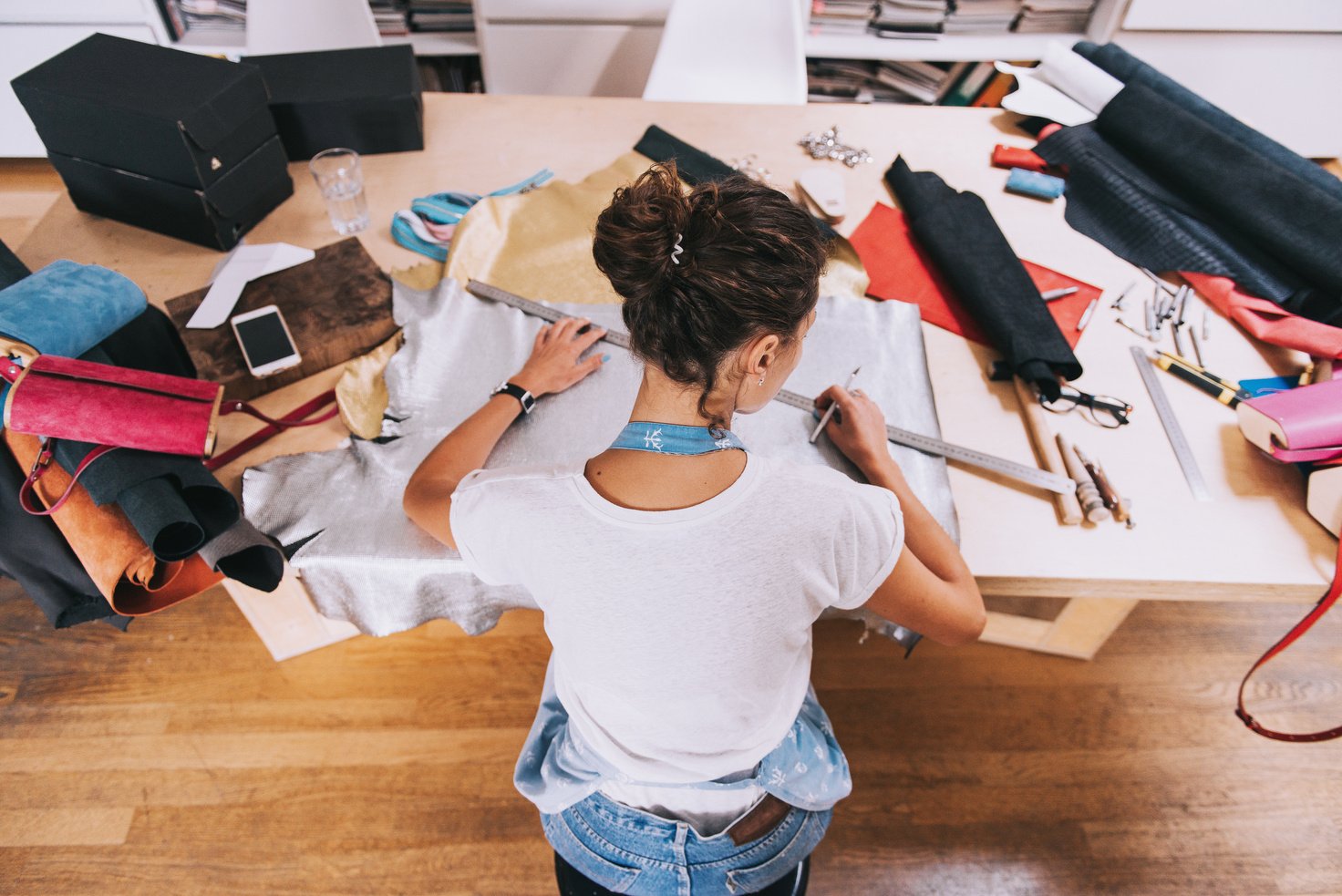 Young female purse maker working with leather textile at her workshop.